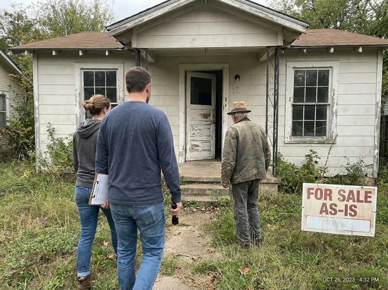 Two local home buyers and a homeowner walking up to an older Austin house with a For Sale As-Is sign in the overgrown front yard