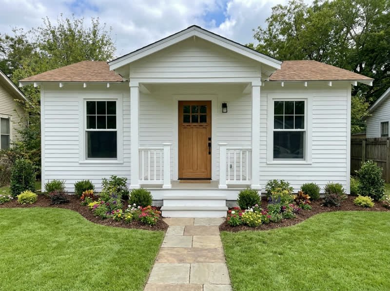Restored white bungalow with a new porch, fresh flower beds, and a stone walkway